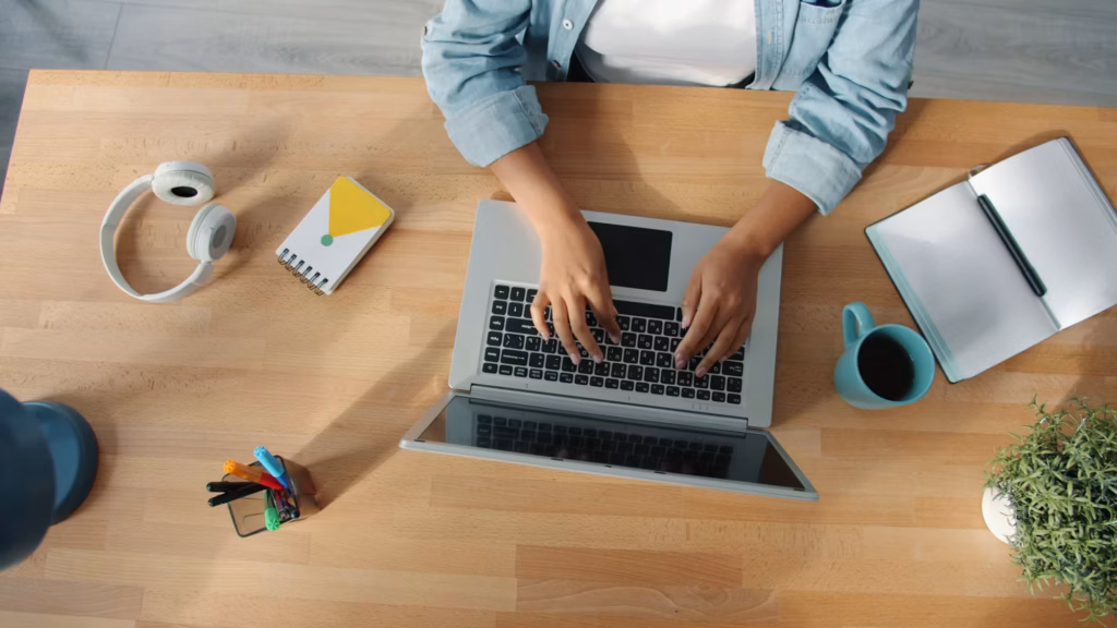 Personne travaillant sur un ordinateur portable à un bureau en bois, en train de rédiger une requête à un outil d'intelligence artificielle